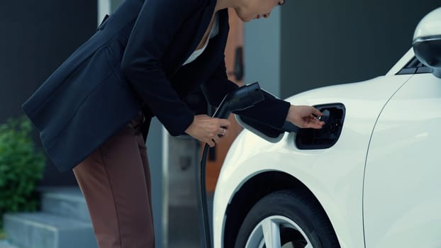 A woman unplugs the electric vehicle's charger at his residence. Concept of the use of electric vehicles in a progressive lifestyle contributes to a clean and healthy environment.