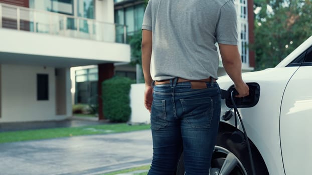 Progressive man attaches an emission-free power connector to the battery of electric vehicle at his home. Electric vehicle charging via cable from charging station to EV car battery