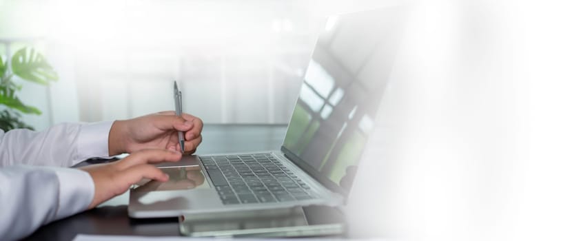 Businessman holding a pen and using a computer to work sits in a modern office with copy space.