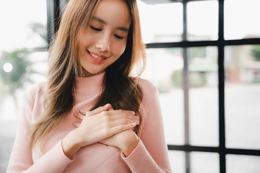 Happy charming female smiling hold hands chest near heart honest with grateful gesture, Beauty Asian young woman touching her chest for thanking feeling no stress at home, peace of mind concept