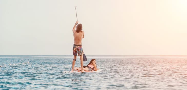 Sea woman and man on sup. Silhouette of happy young woman and man, surfing on SUP board, confident paddling through water surface. Idyllic sunset. Active lifestyle at sea or river