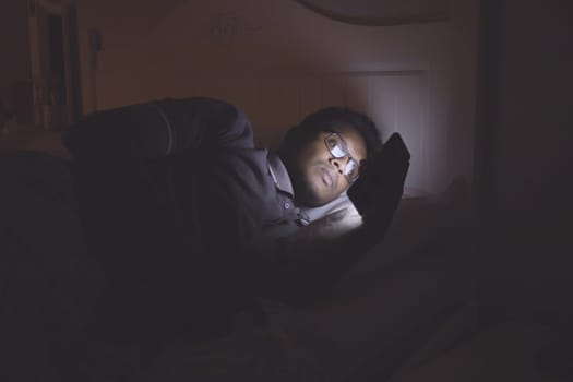 young man sitting on bed using smart phone at night .
