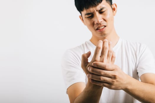 An Asian man, in pain, massages his painful hands and palms. Portrait in a studio shot isolated on white background, highlighting health care and the concept of arthritis.