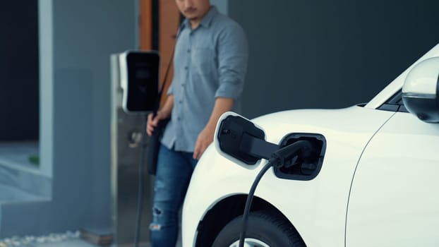 A man unplugs the electric vehicle's charger at his residence. Concept of the use of electric vehicles in a progressive lifestyle contributes to a clean and healthy environment.