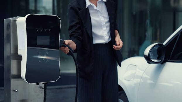 Progressive businesswoman unplug charger plug from charging station to his electric car before driving around city center. Eco friendly rechargeable car powered by sustainable and clean energy.