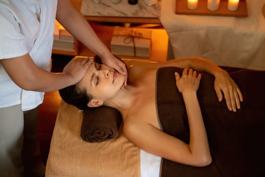 Caucasian woman enjoying relaxing anti-stress head massage and pampering facial beauty skin recreation leisure in warm candle lighting ambient salon spa in luxury resort or hotel. Quiescent