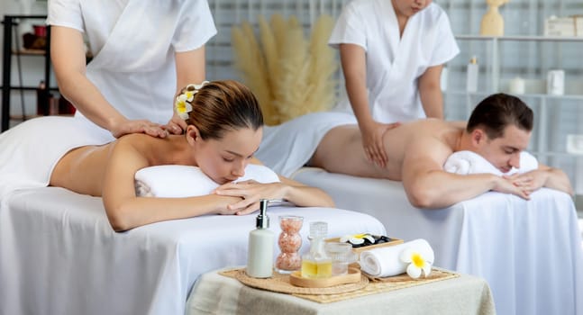 Caucasian couple customer enjoying relaxing anti-stress spa massage and pampering with beauty skin recreation leisure in day light ambient salon spa at luxury resort or hotel. Quiescent