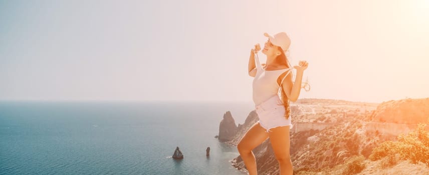 Woman travel sea. Young Happy woman in a long red dress posing on a beach near the sea on background of volcanic rocks, like in Iceland, sharing travel adventure journey