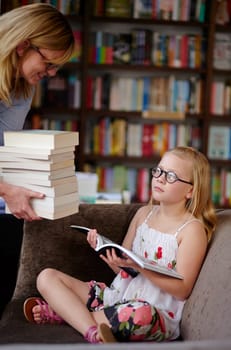 Reading, books and woman with child in library with stack, learning and relax with study knowledge. Storytelling, happy mom and girl in bookstore together with story, fantasy and education on couch