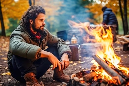 A male traveler sits by a fire in the forest. High quality photo