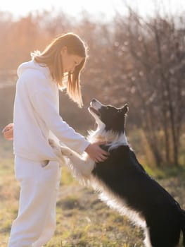 Caucasian woman hugging her dog Border Collie while sitting on a bench in autumn park