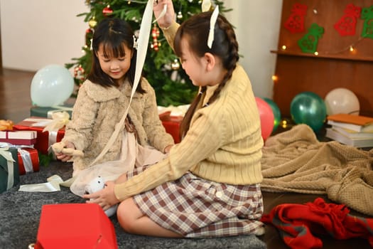 Happy little sisters opening Christmas gift in beautifully decorated living room. Holidays and childhood concept.