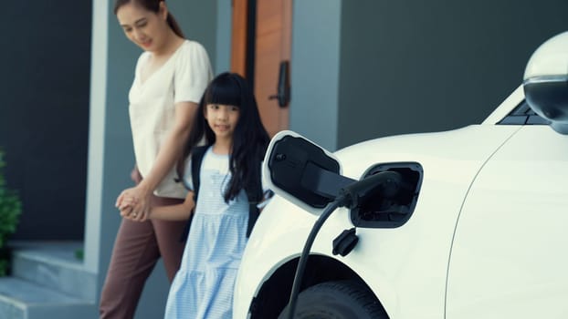 Progressive lifestyle of mother and daughter who have just returned from school in an electric vehicle that is being charged at home. Electric vehicle powered by sustainable clean energy.