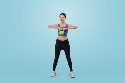 Vigorous energetic woman doing kettlebell weight lifting exercise on isolated background. Young athletic asian woman strength and endurance training session as body workout routine.