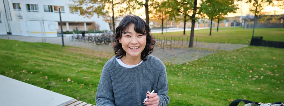 Young girl, korean artist or art student sits in park with digital tablet, draws with graphic pen, scatches a design or project, looks around.