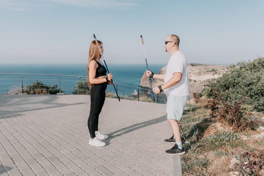 Happy Middle aged couple or friends practicing nordic walking in park near sea. Mature couple with trekking poles walking, practicing Nordic walking outdoors. Aging youthfully and sport concept.