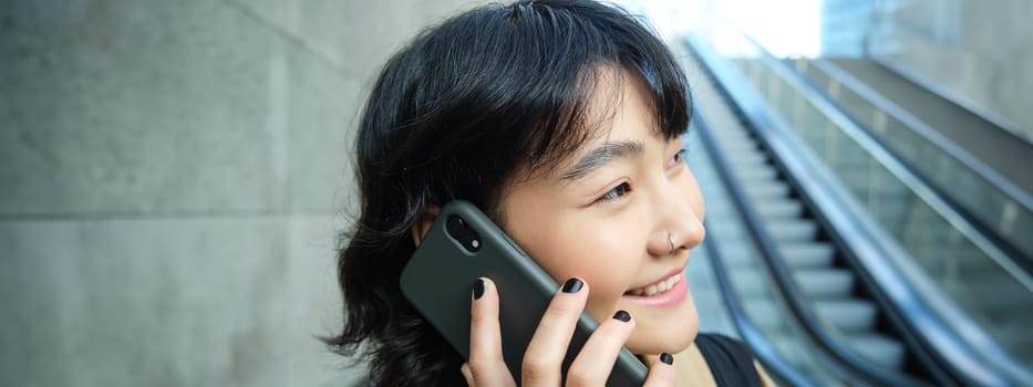 Headshot of smiling korean woman with smartphone, makes a phone call, goes down escalator in city, commutes to university.