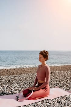 Middle aged well looking woman with black hair doing Pilates with the ring on the yoga mat near the sea on the pebble beach. Female fitness yoga concept. Healthy lifestyle, harmony and meditation.