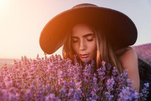 Close up portrait of young beautiful woman in a white dress and a hat is walking in the lavender field and smelling lavender bouquet.