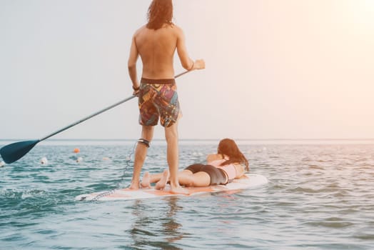 Sea woman and man on sup. Silhouette of happy young woman and man, surfing on SUP board, confident paddling through water surface. Idyllic sunset. Active lifestyle at sea or river