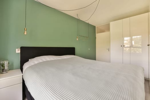 a bed in a room with green walls and white cupboards on the wall behind it is a black headboard