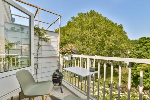 a balcony with two chairs and a grill on the left side, in front of a white fenced area