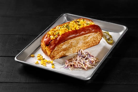 Appetizing hot dog in toasted brioche sandwich bread with smoked sausage, cheese topped with corn salsa and pumpkin seeds with light mayo served with pickles and shredded cabbage