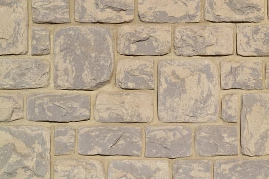 A beige stone wall with big and small stones on a big house.