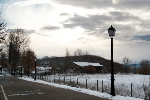 Public lamp by sunrise at countryside covered with snow