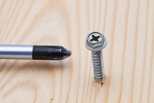 Screwdriver and screw on wood background