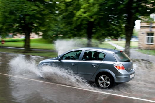 A car splashes through a large puddle on a wet road.