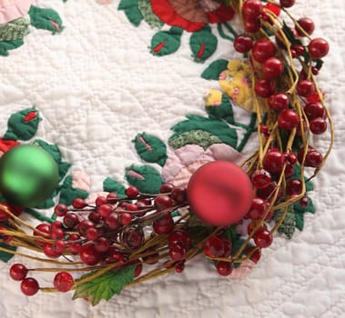 Christmas wreath with red berries and ornaments on a colorful quilt with copy space