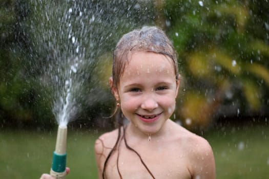 Happy girl pours water from a hose