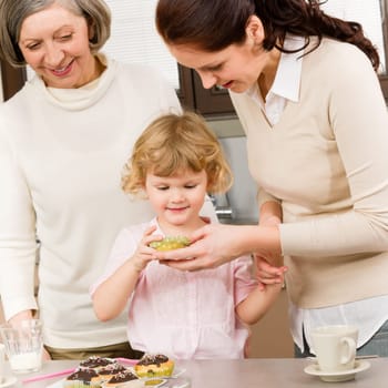 Three generations women around cupcake little girl tasting cookies