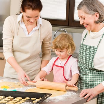 Happy little girl rolling out dough with mum and grandmother