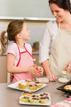 Mother and daughter decorating cupcakes sprinkles happy together at home