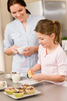 Little girl taste sprinkles cupcakes with mum happy at home