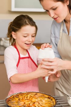 Mother and daughter decorating apple pie with sugar icing