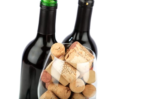 Glass with wine cork in front of two bottles of wine