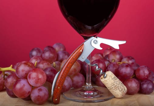 Corkscrew with cork stands in front of red wine glass