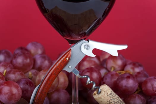 Corkscrew with cork stands in front of red wine glass