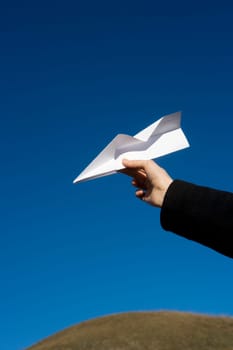Hand holding a Paper Airplane towards blue sky