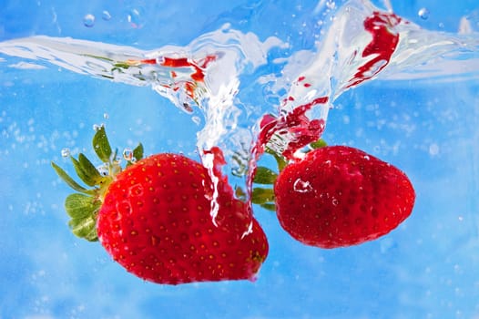 Fresh strawberries falling into the water on a blue mosaic background