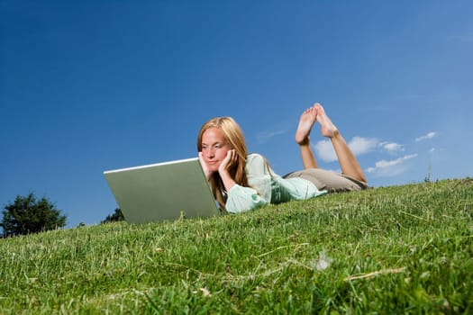 Woman with computer in the grass towards blue sky