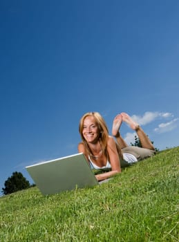 Woman with computer in the grass towards blue sky