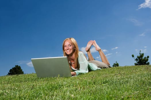 Woman with computer in the grass towards blue sky