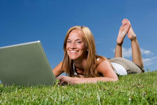 Woman with computer in the grass towards blue sky