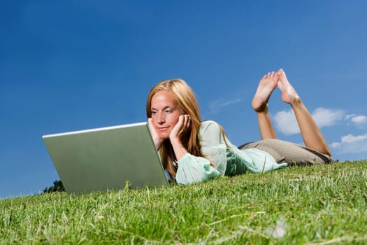 Woman with computer in the grass towards blue sky