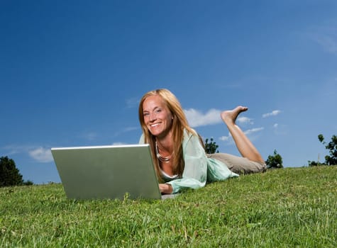 Woman with computer in the grass towards blue sky
