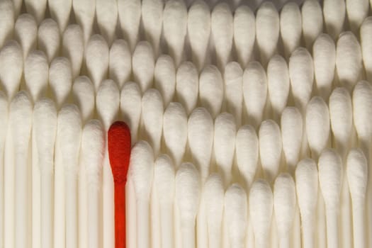 A red cotton bud on top of a whole lot of white cotton buds